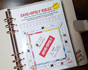 May include: A planner with a "Save-Opoly Rules" game board insert. The game board has spaces for tracking savings, with text that reads "Crush Your Goalz" on the planner cover. The planner is open to the game board.