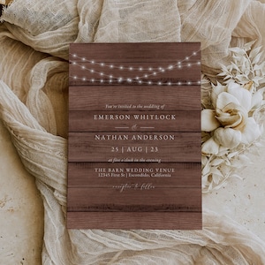 May include: Rustic wedding invitation with string lights on a wood background. The invitation reads "You're invited to the wedding of Emerson Whitlock & Nathan Anderson 25 AUG 23 at five o'clock in the evening The Barn Wedding Venue 12345 First St | Escondido, California"