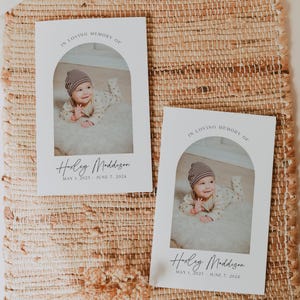 May include: Two white rectangular memorial cards featuring an arched photo of a baby wearing a striped hat and patterned outfit. The text reads IN LOVING MEMORY OF, the name Huxley Maddison, and the dates MAY 1, 2023 - JUNE 7, 2024.