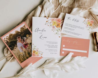 May include: A wedding invitation suite featuring a photo card of a couple in a field, a main invitation with floral accents and the text Amelia and Lucas, a details card, and a coral reply card. The set includes white paper stationery.