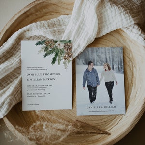Puede incluir: Juego de papeler&iacute;a de boda con una invitaci&oacute;n y una tarjeta fotogr&aacute;fica. La invitaci&oacute;n presenta texto y un dise&ntilde;o bot&aacute;nico con pi&ntilde;as y vegetaci&oacute;n. La tarjeta fotogr&aacute;fica muestra a una pareja en la nieve. Ambos est&aacute;n en una bandeja de madera.