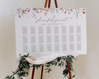 May include: A white wedding seating chart sign on a wooden easel, featuring a floral border at the top, the text "please find your seat," "ASHLEY + ADAM | SEPTEMBER 21, 2022," and a list of guest names organised by table numbers 1 through 24.