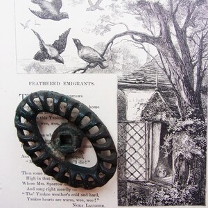 May include: An antique, dark green metal oval-shaped object with a spiral design, resting on a vintage book page with illustrations of birds and a cottage. The text "FEATHERED EMIGRANTS" is visible.