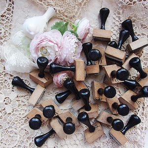 May include: A collection of vintage wooden stamps with black handles, scattered on a lace surface. Soft pink flowers and a white bird figurine add a touch of elegance. The stamps have various letter imprints.