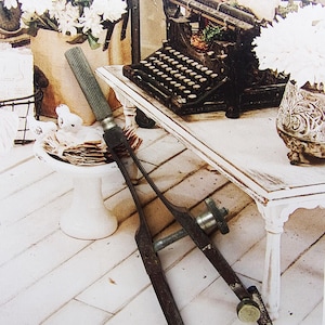 May include: An antique drafting compass with a screw adjustment, set against a backdrop of a vintage typewriter and white flowers. The compass is made of dark metal and has a worn, aged appearance. The scene evokes a sense of nostalgia and craftsmanship.