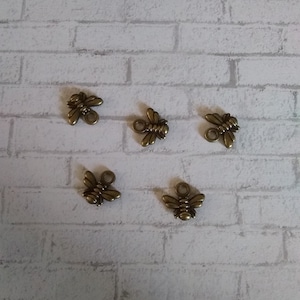 May include: Five gold-toned bee charms with a loop for attaching to a necklace or bracelet.