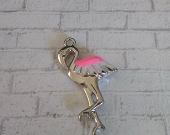 May include: A silver-colored flamingo charm with a pink breast and white wing feathers. The charm has a loop at the top for attaching to a necklace or bracelet. The flamingo is standing on one leg.