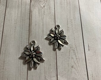 May include: Two silver metal charms in the shape of a poinsettia flower. The charms have a detailed design with a raised center and petals.