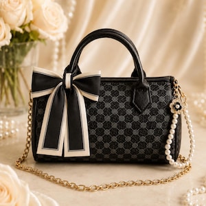May include: A black barrel-shaped handbag featuring a repeating circular logo pattern, a black and white ribbon bow on the front, two top handles, and a gold-tone chain strap accented with a string of white faux pearls and a small flower charm.
