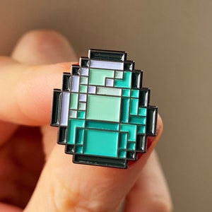 May include: A green and blue enamel pin shaped like a Minecraft diamond block.
