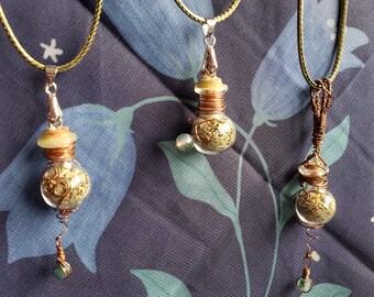 May include: Three necklaces with glass vials filled with dried herbs and a small gemstone pendant. The vials are suspended from a silver or copper wire and the necklaces are made with a green cord.