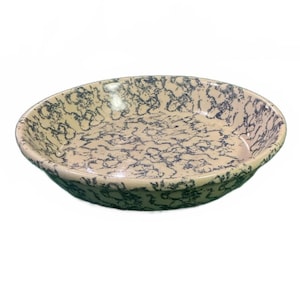 Puede incluir: Una fuente ovalada de cerámica con una base color crema y un patrón moteado azul oscuro. El borde y la parte inferior de la fuente también son de color azul oscuro. La fuente probablemente se utiliza para servir alimentos.