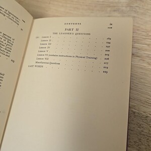 K&ouml;nnte beinhalten: Aufgeschlagenes Buch mit Inhaltsverzeichnis. Der Titel "PART II THE LEARNER'S QUESTIONS" ist zu sehen. Lektionstitel und Seitenzahlen sind aufgelistet. Das Buch liegt auf einer Holzoberfl&auml;che.