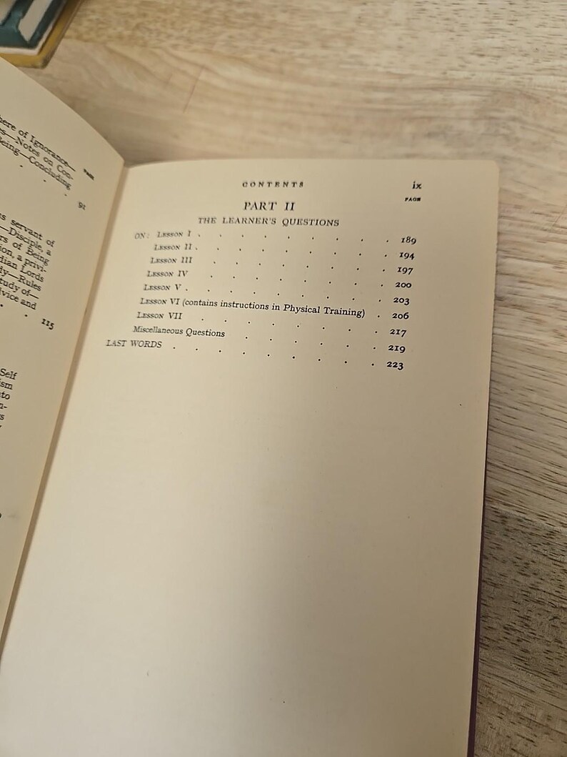 K&ouml;nnte beinhalten: Aufgeschlagenes Buch mit Inhaltsverzeichnis. Der Titel "PART II THE LEARNER'S QUESTIONS" ist zu sehen. Lektionstitel und Seitenzahlen sind aufgelistet. Das Buch liegt auf einer Holzoberfl&auml;che.