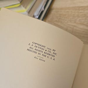 K&ouml;nnte beinhalten: Aufgeschlagene Buchseite mit Text: "COPYRIGHT, 1939, BY E. P. DUTTON & CO., INC. ALL RIGHTS RESERVED PRINTED IN THE U. S. A. First Edition." Die Seite ist cremefarben, mit anderen Buchseiten im Hintergrund.