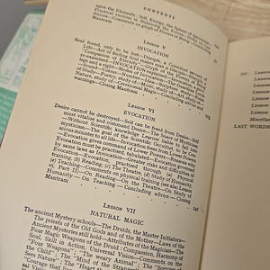 K&ouml;nnte beinhalten: Aufgeschlagenes Buch mit Texten &uuml;ber Beschw&ouml;rung, Evokation und Naturmagie. Die Seiten sind vergilbt, und der Text enth&auml;lt &Uuml;berschriften wie 'Lektion V' und 'Lektion VI' mit detaillierten Erkl&auml;rungen und Unterpunkten.