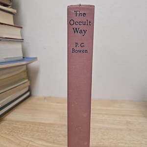 K&ouml;nnte beinhalten: Ein Vintage-Buch mit dem Titel "The Occult Way" von P.G. Bowen. Das Buch hat einen staubrosafarbenen Einband mit dem Titel und dem Namen des Autors in dunkler Schrift. Der Name des Verlags, Dutton, steht unten. Das Buch steht auf einer Holzoberfl&auml;che.