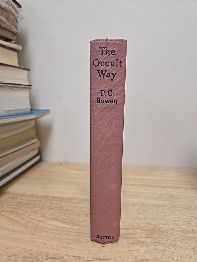 K&ouml;nnte beinhalten: Ein Vintage-Buch mit dem Titel "The Occult Way" von P.G. Bowen. Das Buch hat einen staubrosafarbenen Einband mit dem Titel und dem Namen des Autors in dunkler Schrift. Der Name des Verlags, Dutton, steht unten. Das Buch steht auf einer Holzoberfl&auml;che.