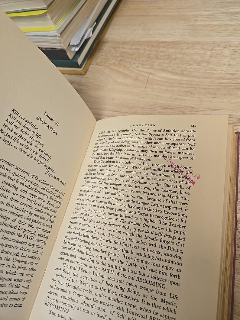 K&ouml;nnte beinhalten: Offenes Buch mit gealterten, vergilbten Seiten. Schwarzer Text f&uuml;llt die Seiten, mit der Kapitel&uuml;berschrift "Evocation" sichtbar. Der Text behandelt Okkultismus und Spiritualit&auml;t. Ein Stapel B&uuml;cher ist im Hintergrund zu sehen.