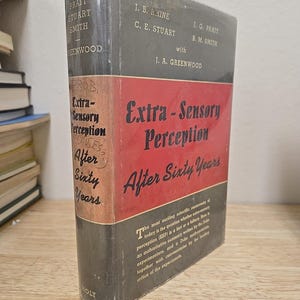 May include: A hardcover book titled "Extra-Sensory Perception After Sixty Years." The book has a red and black cover with the title in large, bold letters. The spine is gray with author names. The book is wrapped in clear plastic.