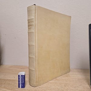 May include: A vintage book titled "FRARD'S HERBALL 1927" with a cream-colored cover and spine. The spine has raised bands. A small blue and white eraser is next to the book.
