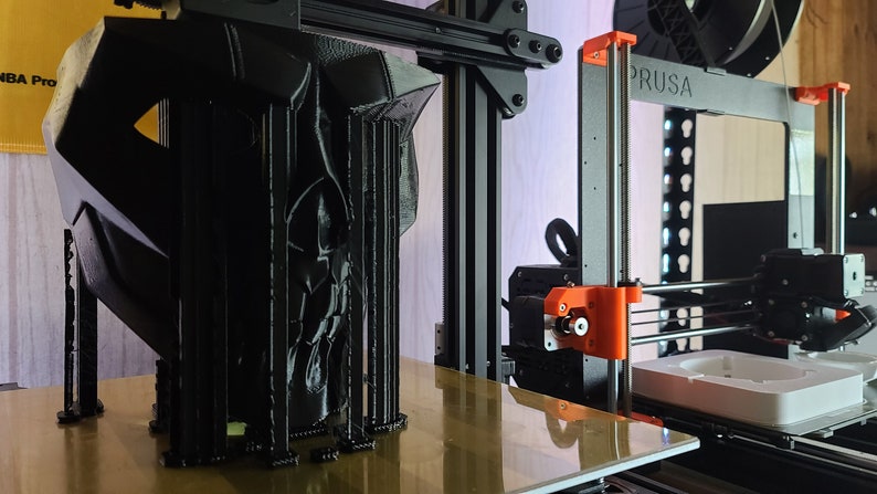 K&ouml;nnte beinhalten: Ein schwarzes 3D-gedrucktes Objekt mit filigranen Details wird auf einem Prusa 3D-Drucker gedruckt. Das Objekt befindet sich auf einer Plattform und der Drucker ist in Betrieb.