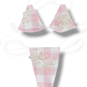 Könnte beinhalten: Ein zweiteiliges Dessous-Set mit rosa-weißem Vichy-Muster. Das Triangel-Oberteil und der String-Slip sind mit zarten, perlenbesetzten Blumenverzierungen versehen. Das Set wird von dünnen, weißen Schnüren gehalten.