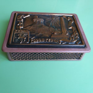 May include: A brown and black matchbox with a raised image of a city skyline and the text "Город-Герой" (Hero City).