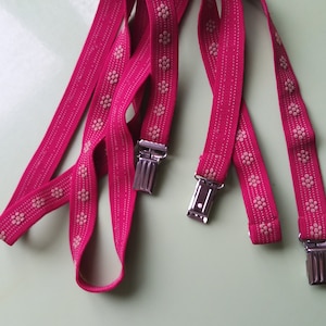 May include: Pink suspenders with white polka dots and silver clips.