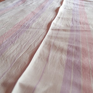 May include: A white bedspread with pink and purple stripes. The bedspread is made of a soft, textured fabric.
