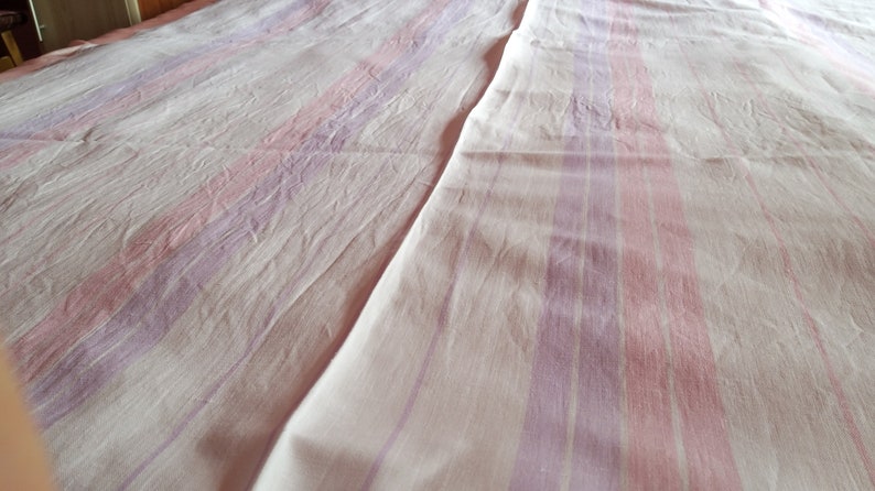 May include: A white bedspread with pink and purple stripes. The bedspread is made of a soft, textured fabric.