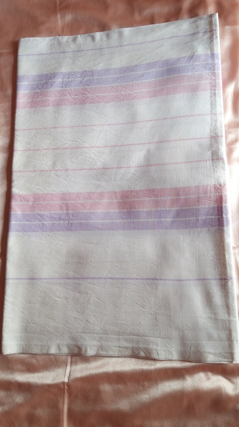 May include: A white fabric sheet with pink and purple stripes. The sheet is folded and lying on a peach-coloured surface.