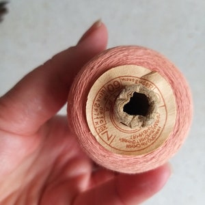 May include: A spool of pink thread with a label that reads "K.I.C. 711 22 PIC. A 600", "СОВ. ПРОМ.", and "ХЛОПЧАТОБУМАЖНЫЕ НИТИ ДУБЛ.  №1".