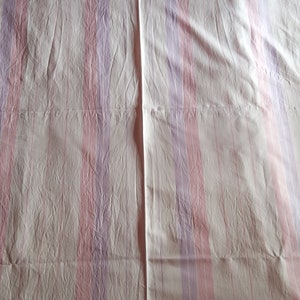 May include: White bed sheet with pink and purple stripes. The sheet is creased and has a seam down the middle.