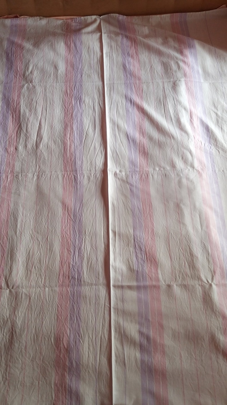 May include: White bed sheet with pink and purple stripes. The sheet is creased and has a seam down the middle.