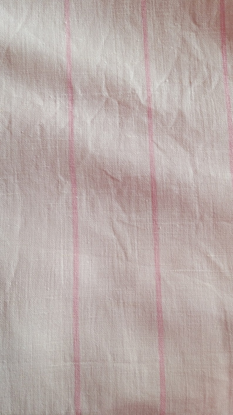 May include: White fabric with thin pink stripes. The fabric has a subtle texture and is slightly wrinkled.