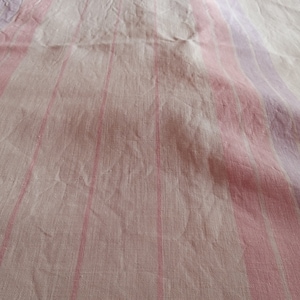 May include: White linen fabric with pink and purple stripes. The fabric is creased and has a textured surface.