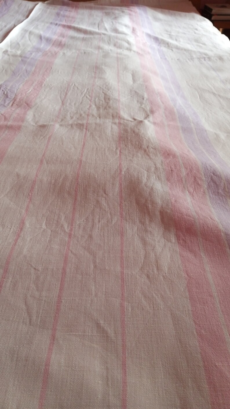 May include: White linen fabric with pink and purple stripes. The fabric is creased and has a textured surface.