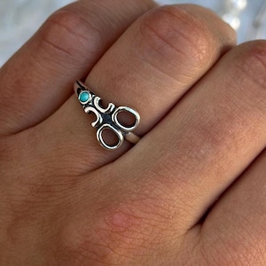 May include: A white ceramic mug with a black handle and the text "But First, Coffee" in a bold, black font. The mug is set against a blurred background, suggesting a cozy setting.