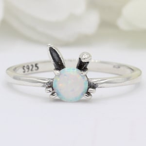 May include: A silver ring with a white opal stone and a bunny rabbit design. The ring is marked "S925" on the band.