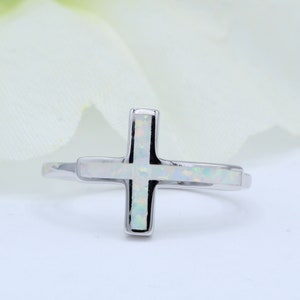 Puede incluir: Un anillo de plata con un diseño de cruz de ópalo blanco.
