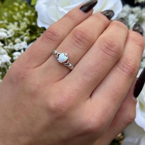 May include: A silver ring with a white heart-shaped opal stone and a Celtic knot design.