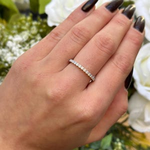 May include: A thin silver band with a row of small, round, clear gemstones.