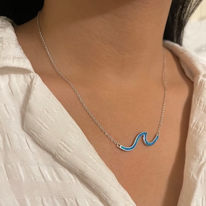 May include: A silver chain necklace with a blue opal wave pendant.
