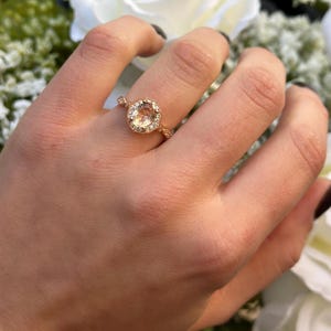 May include: A rose gold engagement ring with a large oval-shaped center stone and a halo of smaller diamonds. The band is twisted and features delicate details.