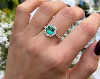 Könnte beinhalten: Ein silberner Ring mit einem grünen Edelstein, der von kleineren Diamanten umgeben ist. Der Ring befindet sich an einem Finger.