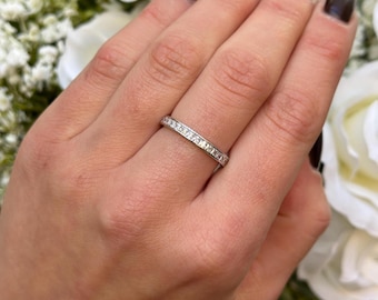 May include: A silver band ring with a row of small, square-shaped clear stones set in a continuous line around the band.