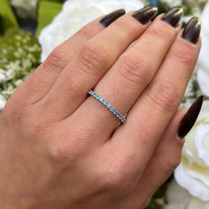 May include: A delicate eternity band ring with a row of small, light blue gemstones set in a silver band.