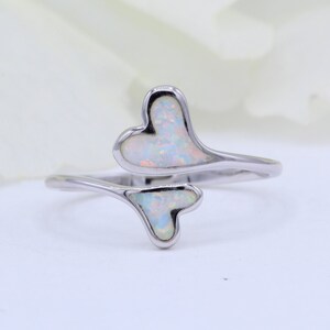 May include: A silver ring with two white opal hearts. The hearts are connected by a silver band.