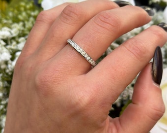 Puede incluir: Una fina banda de plata con una fila de pequeños diamantes transparentes engastados en pavé.